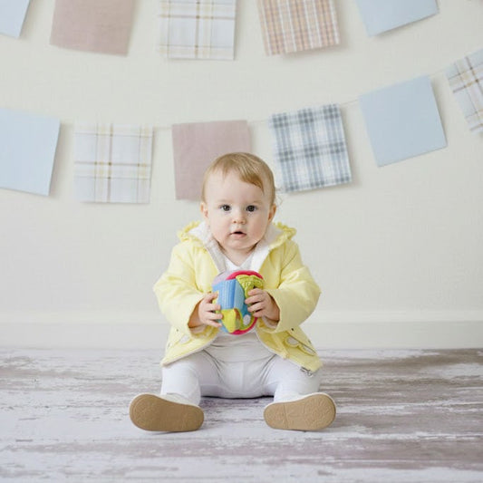 Baby sitting on the floor holding a colorful toy with decorative square patterns on the wall.
